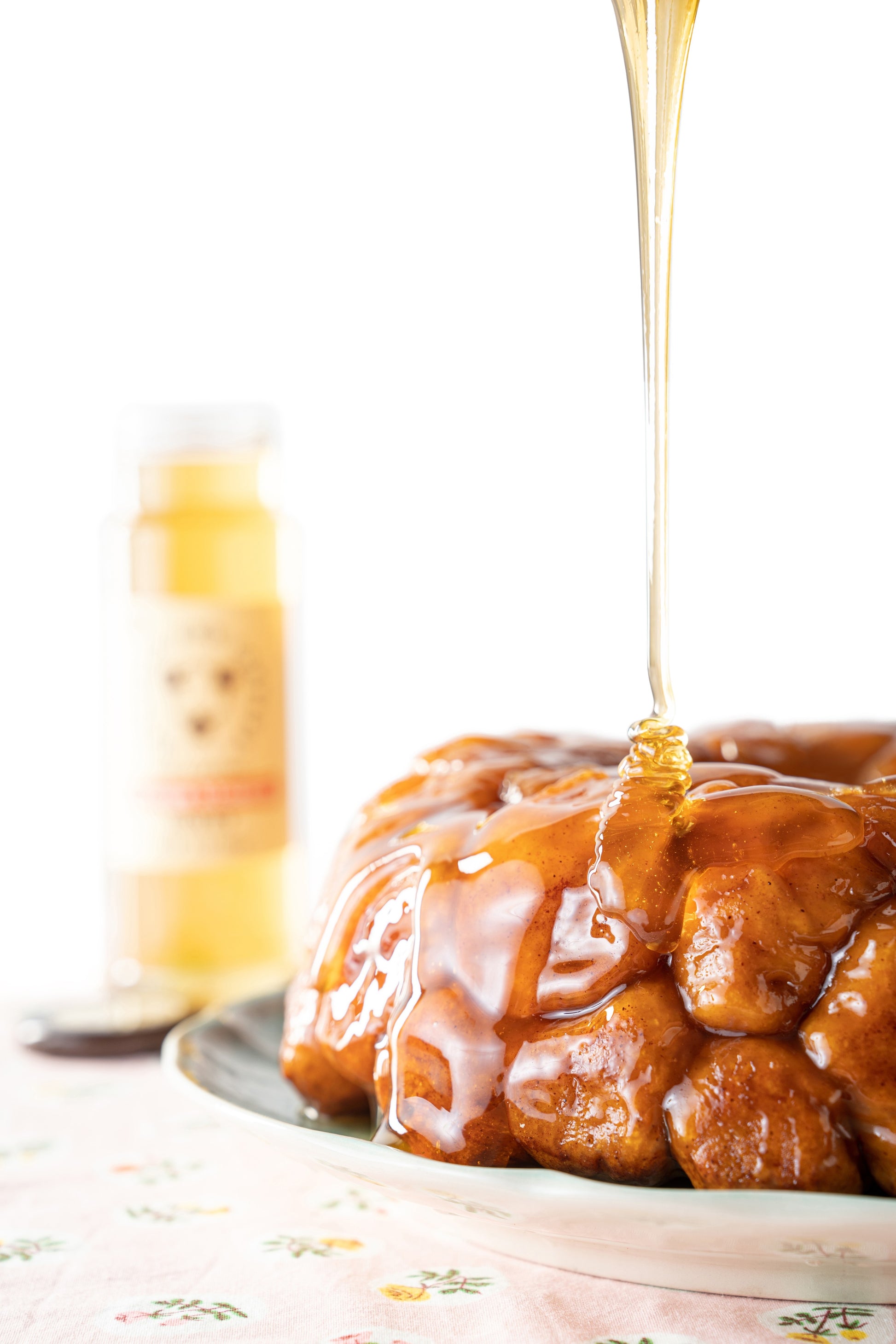 Monkey bread on a plate being drizzled with orange blossom honey with the 12 ounce jar in the background.