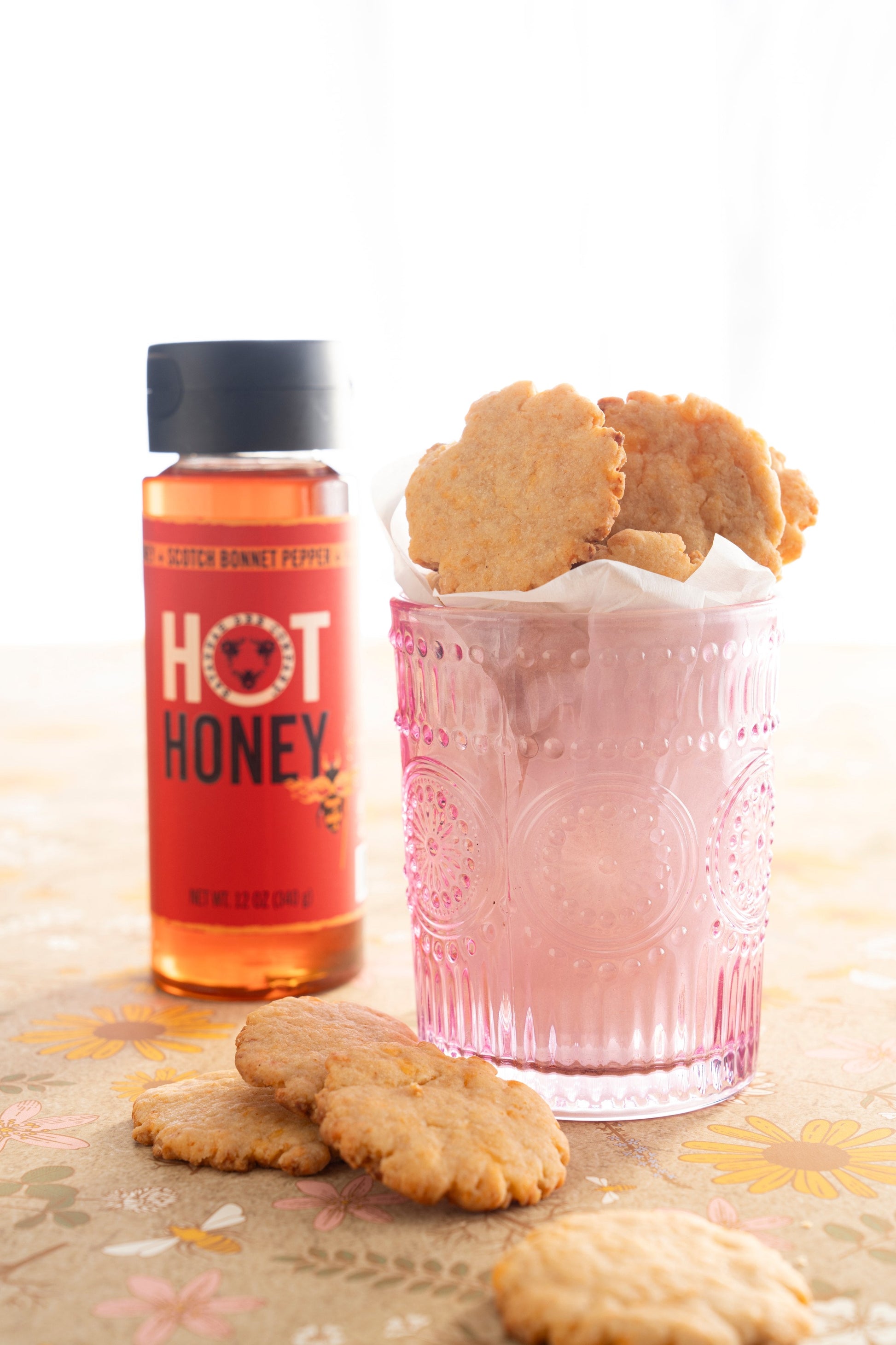 Hot honey squeeze bottle next to a cup full of hot honey biscuits.